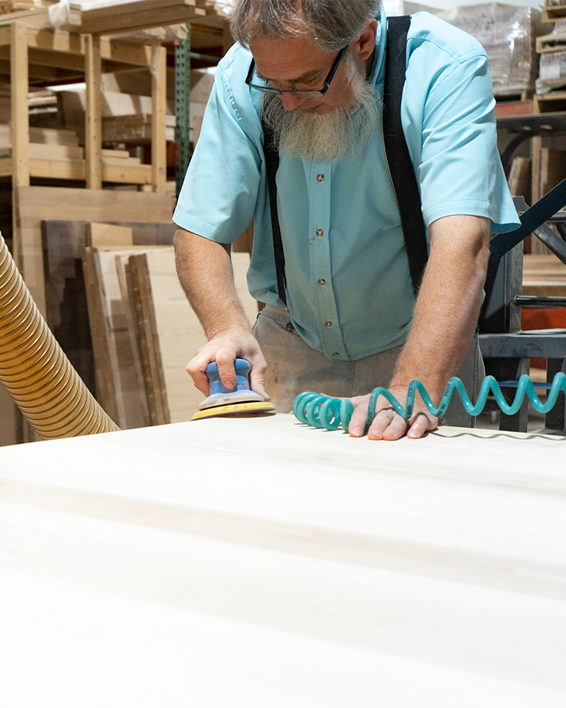 Amish craftsman sanding solid wood furniture by hand.
