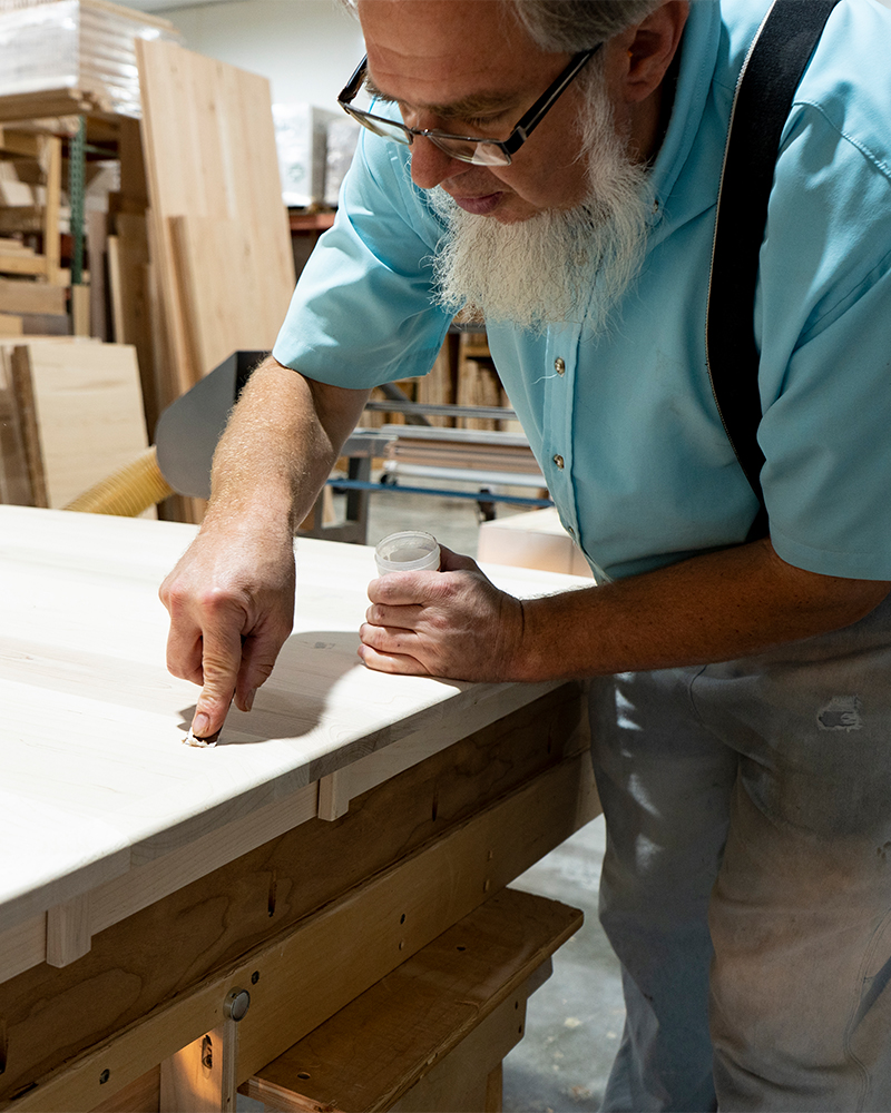 Amish craftsman applying wood filler to handcrafted furniture.