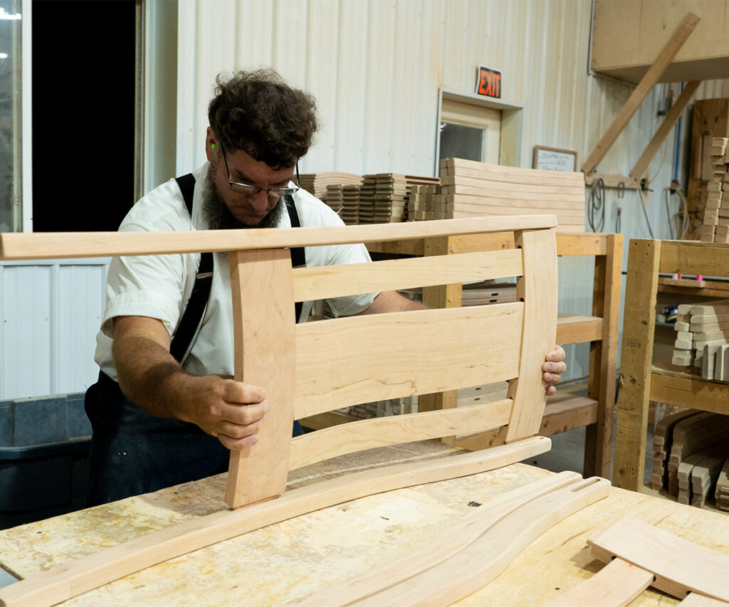 Amish craftsman aligning hardwood headboard frame during furniture assembly for square, consistent fit.