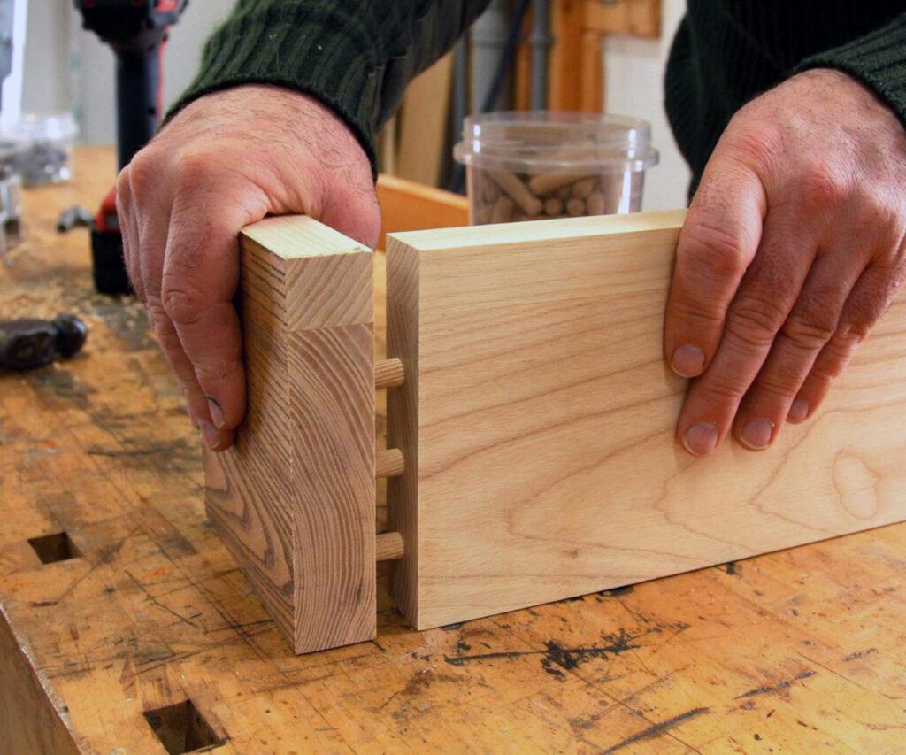 Hands fitting dowel joinery on hardwood boards, showing Amish furniture strength.