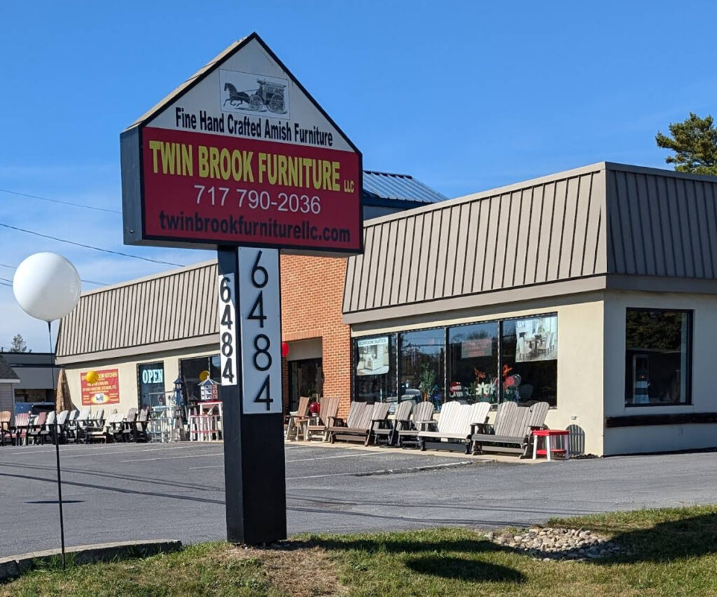 Twin Brook Furniture Amish showroom exterior with roadside sign and outdoor chairs.